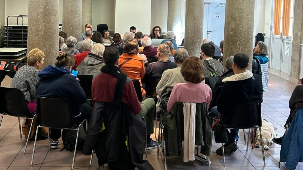 les participants à l'AG assis de dos face à la tribune occupée par le bureau