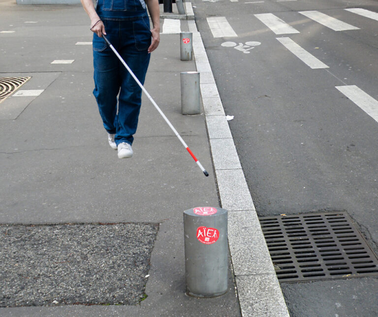 personne se déplaçant à la canne face à nous prête à buter sur un plot mal placé sur le trottoir
