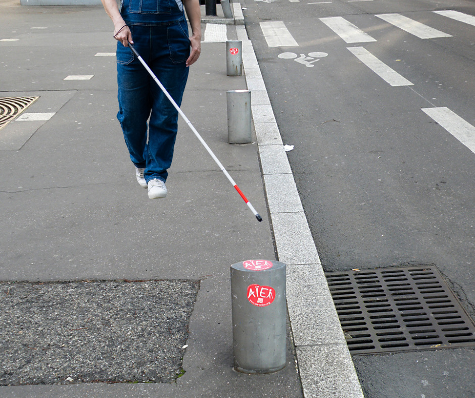 personne se déplaçant à la canne face à nous prête à buter sur un plot mal placé sur le trottoir