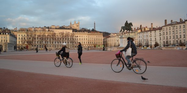 Vélos traversants la place Bellecour avec vue sur Fourvière